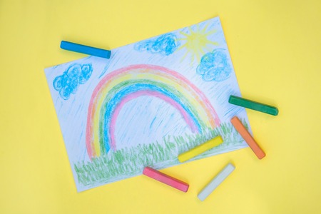 Children's drawing with colorful rainbow on a piece of paper with crayons on a bright yellow backgroundの写真素材