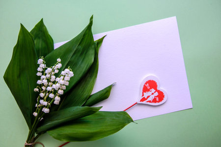 Lily of the valley bouquet, white paper and wooden heart on a stick on a green background