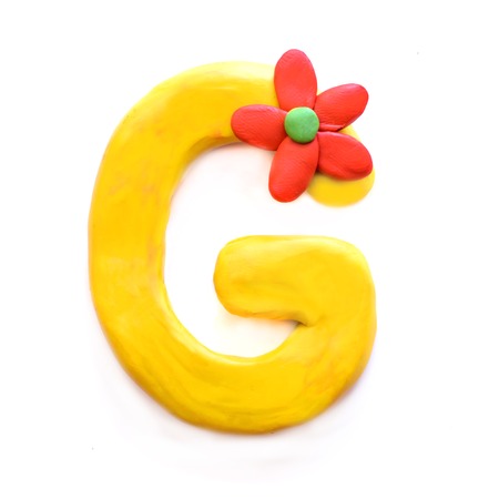 Yellow plasticine letter G English alphabet with red flower, isolate on white backgroundの写真素材