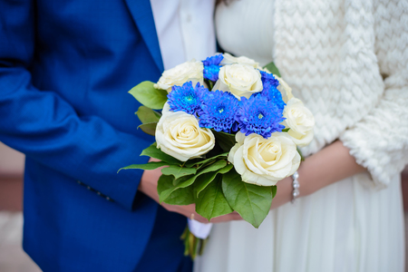 Beautiful wedding bouquet of blue and white flowers close up in the hands of the bride and groomの写真素材