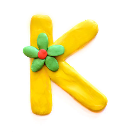 Yellow plasticine letter K with green flower, isolate on white backgroundの写真素材