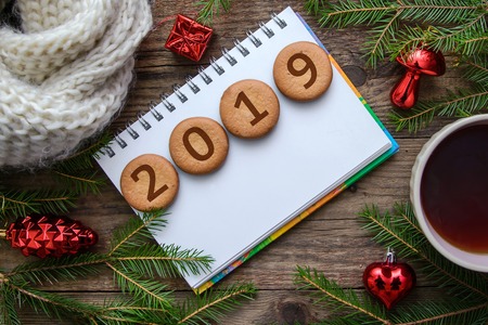 New Year picture with Christmas tree branches and the number 2019 on round cookies with a cup of hot tea on a wooden backgroundの写真素材