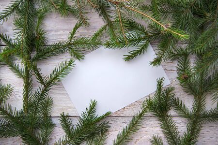 Frame of green Christmas tree branches and a sheet of paper on a white wooden background, copy spaceの写真素材