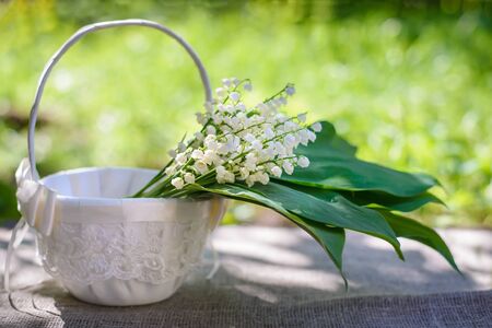 Spring bouquet of lilies of the valley with green leaves in a beautiful white basket with laceの写真素材