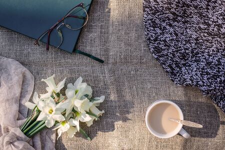 Layout with flowers daffodils, a book and glasses, tea, coffee with milk on a canvas backgroundの写真素材
