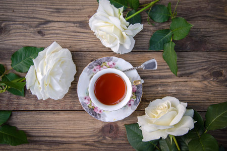 Three beautiful white roses and a cup of tea on a rustic wooden background