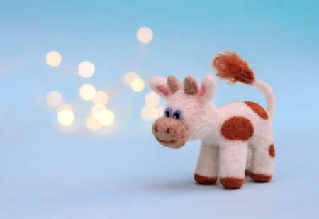 Symbol of 2021, a toy felt bull or cow on a festive light blue background with bokeh, with a copy spaceの写真素材