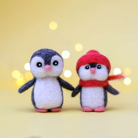 Two Christmas toy felted wool cute little penguins on a yellow background with bokehの写真素材