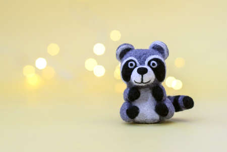 Christmas toy felted wool cute little raccoon on a yellow background with bokeh, copy spaceの写真素材