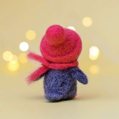 Christmas toy felted wool cute little penguin in a winter red hat and scarf, standing with her back, on a yellow background with bokeh, copy spaceの写真素材