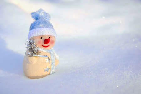 A cute toy snowman in a blue cap on the snow in winterの写真素材