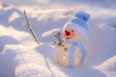 A cute toy snowman in a blue cap on the snow in winterの写真素材
