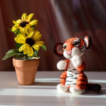 Cute toy tiger sitting next to yellow flowers, symbol of the year 2022, felting woolの写真素材