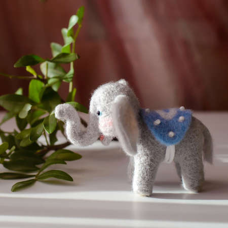 Cute woolly toy elephant under green leaves on a sunny day, felting woolの写真素材