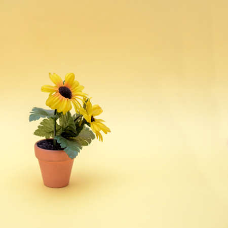 A pot with artificial flowers and leaves on a yellow background, copy spaceの写真素材