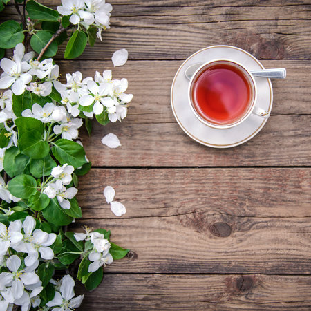 Spring layout with white flowers a blooming apple tree branch and a cup of tea on a wooden...