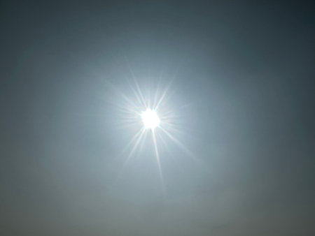 Glowing sun radiating light with sunbeams and lens flares. Sun with smokey sky background. Light creating shimmering rays.の写真素材