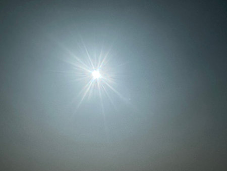 Bright sun shining through hazy sky. Sunlight filtering atmosphere creating ethereal effect with...