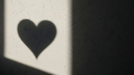 Heart shadow on textured wall. Light and dark contrast on rough surface. Romantic symbol in abstract light. Minimalist design, simple background. Love concept, emotional feeling. Sunlight reflection, room interior, home decor, modern art, graphic element.の素材