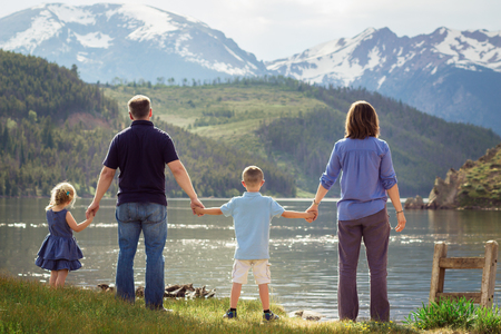 back of family holding hands looking at lake and mountainsの写真素材