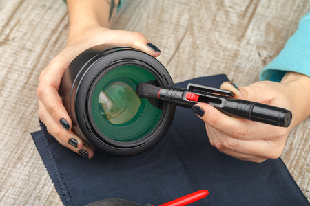 The photographer cleans the lens of dust on a wooden table. Close-up. Studio Lightingの写真素材