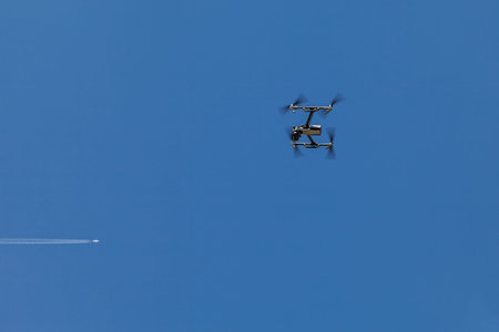 A quadrocopter suspended in the air against a blue sky and a flying plane