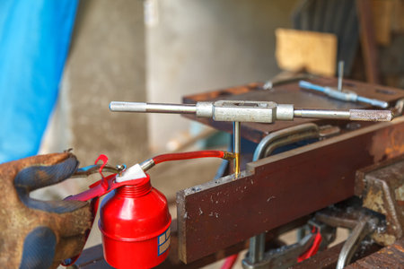 Worker in yellow and blue protective gloves cut the internal thread with a hand tap. Preparing a...
