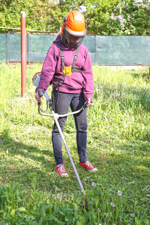 Woman farmer mows the grass in the backyard using string trimmer