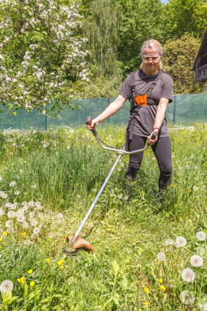 A woman mows grass on his property with a gasoline trimmer