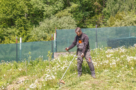 A man mows grass on his property with a gasoline trimmer