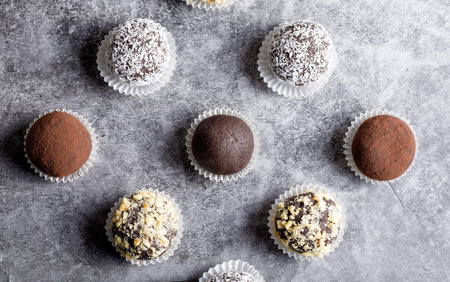 Homemade potato candy with grated cashew nuts, coconut flakes and cocoa powder on a gray background....