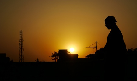 A devotee in silhouette sits on a roof-top, meditating, in an orange sunset in Vrindavana, Indiaの写真素材