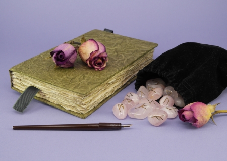 A green journal with dried roses sits next to a black velvet bag of rune stones with a calligraphy pen on a purple background   の写真素材