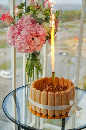 Cooking and decorating Tiramisu cake at home by a master for birthday with a lit candle. Sponge cake...