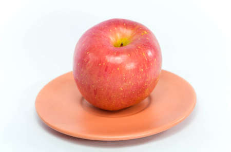 Fresh red apple on an orange dish, white backgroundの写真素材