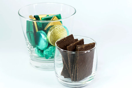 chocolate candy wrapped in colorful foil in a clear glass on  white background
