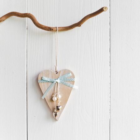 wooden heart hanging on a branch against white wooden planksの写真素材