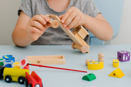 Hands of a child paint a wooden machine