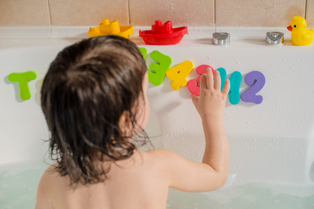 A small child in the bathroom plays with soft and colored letters. Infant training and bathing. Hygiene and care for young children.の写真素材