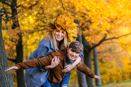 Happy Couple in Autumn Park. Fall. Young Family Having Fun Outdoors. Laughing Man and woman with a wreath of autumn yellow leaves on her headの写真素材