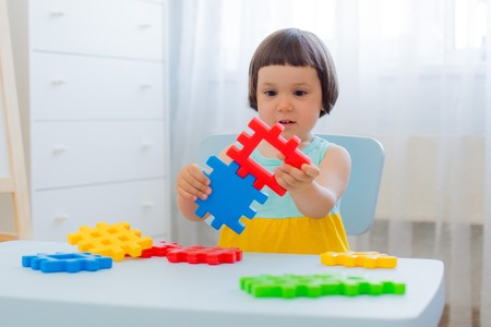 A 3 year old child plays at a table with colorful toy blocks. Children play with educational toys in the kindergarten or room. Preschoolers gather at the table the puzzle out of plastic blocks.の写真素材
