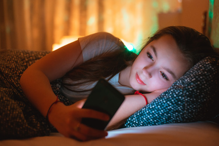 teen girls lying in bed at night and using smartphone. Insomnia and the harm of the smartphone before going to bed. Not healthy sleep. Dependence on social networks in adolescents.の写真素材