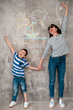 Positive smiling mother and child wearing sunglasses planning her vacation. Sketches of her plans of trip at sea around her concrete wall background drawn son with chalk free space. family holidayの写真素材