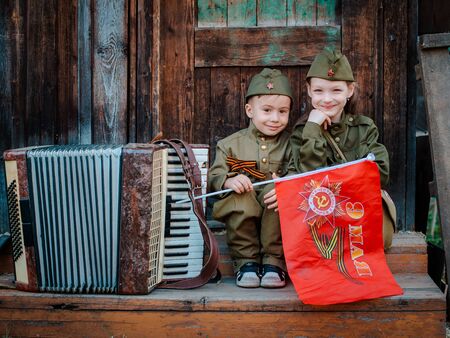 young child in military uniform on holiday day of victory, the scenery of wartime. Rustic style. Accordion, flag. May 9 2018, Russia,のeditorial素材
