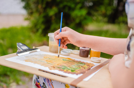 creative artist paints a colorful picture. Close-up of hands and brush in the process of painting outdoors. School of drawing in the open air.の写真素材