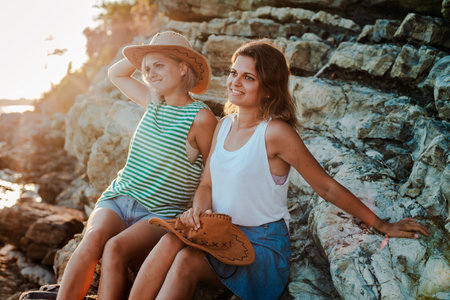 Two young cheerful women in hipsters hats on a rock on the coast of the sea. Summer landscape with...
