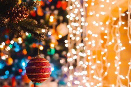 Christmas ball hangs on a decorated fir tree against the background of burning bokeh lights at night. Happy new year greeting card conceptの写真素材