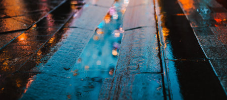 Rainy night in a big city, reflection of colorful city lights on the wet road surface. The view from the street level feet of pedestrians. abstract background. defocused, depth of field, bokehの写真素材