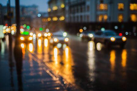 Wet night city street rain Bokeh reflection bright colorful lights puddles sidewalk. Car headlights lighting reflection wet asphalt road Defocused selective focus fuzzy background with red lightsの写真素材