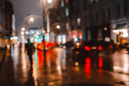 Wet night city street rain Bokeh reflection bright colorful lights puddles sidewalk Car headlights lighting reflection wet asphalt road Defocused selective focus fuzzy background with red lightsの写真素材